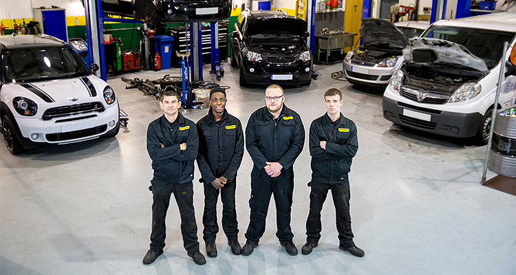 four mechanics standing in a car repair shop