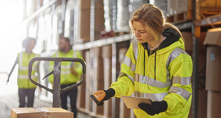 a warehouse worker stands amongst the aisles and scans stock with her hand scanner
