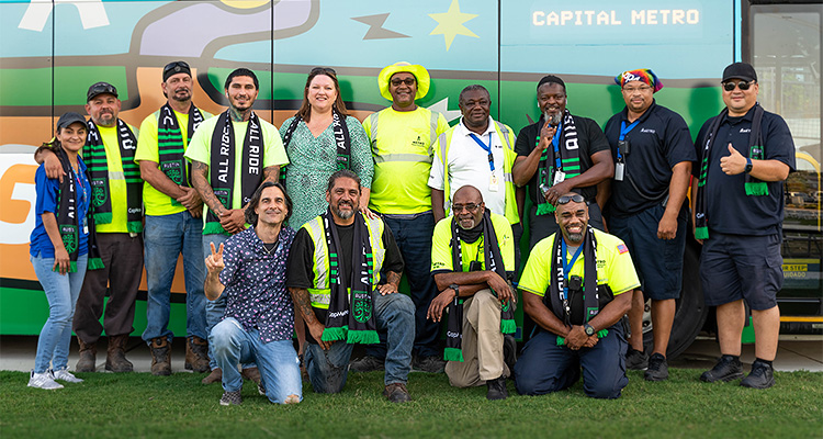 CapMetro, the main public transportation authority in Central, Texas, is committed to increasing regional mobility a group of 13 people posing for a photo in an outdoor setting, standing and kneeling in front of a wall marked with the words "CAPITAL METRO".