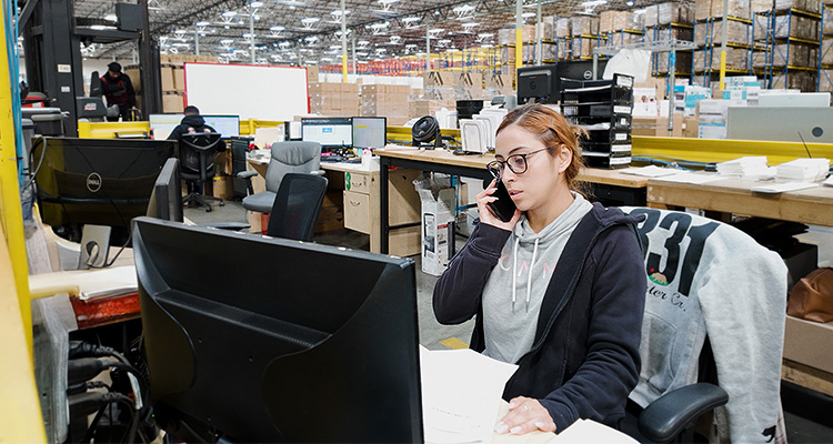oman working at a desk within an office area inside a large industrial warehouse or fulfillment center