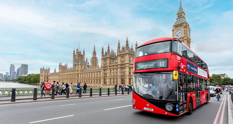 red double-decker bus in London crossing Westminster Bridge, with the Houses of Parliament and Big Ben in the background.