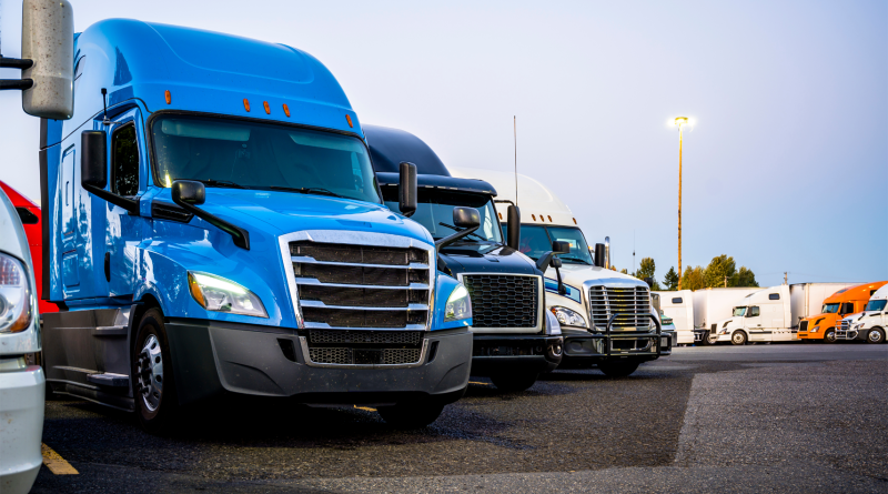 Different big rigs semi trucks standing in row on the truck stop parking lot at evening time