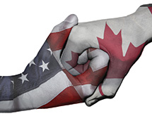 Two hands shaking, one with the American flag on and one with the Canadian flag on.